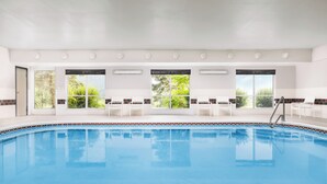 Une piscine à l’eau d’un bleu cristallin, entourée de chaises blanches et bordée de carreaux.