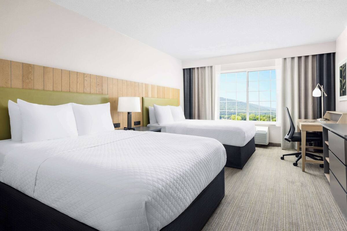 Une chambre d’hôtel avec deux lits, un bureau et une vue sur l’extérieur.