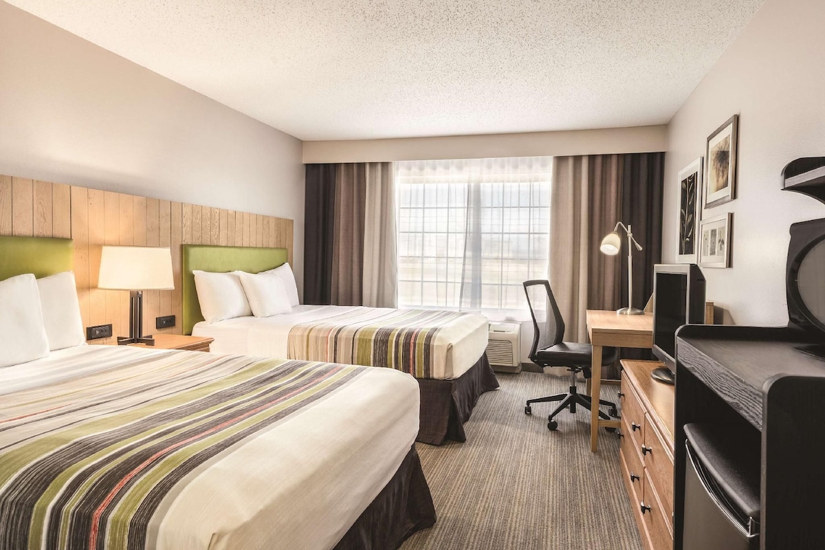 A hotel room with two beds, a desk, a chair, a TV, and a window with curtains.