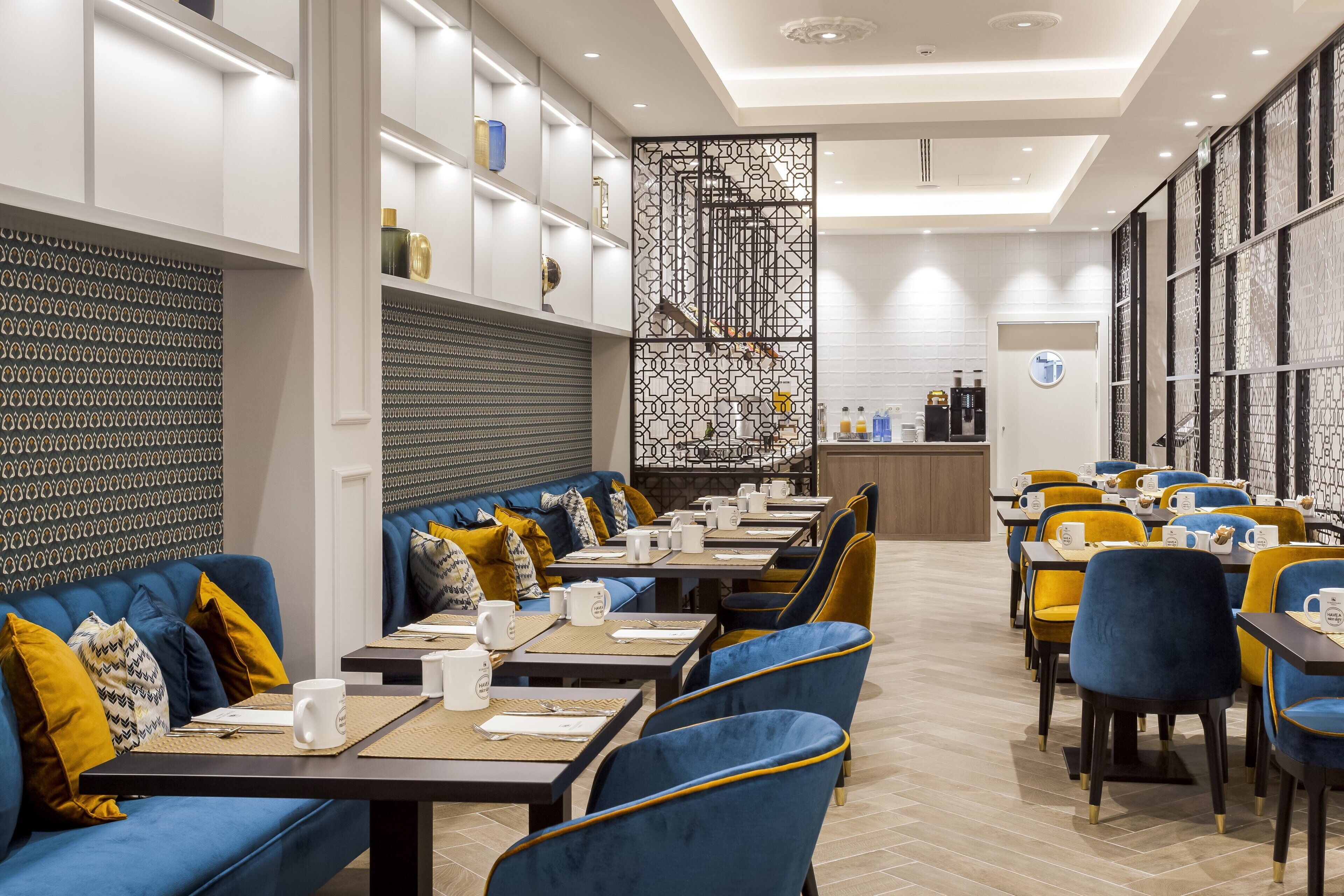 A modern restaurant with blue and yellow seating, white walls, and a patterned divider.