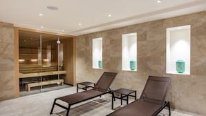 A spa area with two reclining chairs, a wooden bench, and a glass-enclosed sauna. - Eurostars Puerta Real Hotel (Granada)