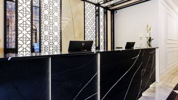 Una mesa de recepción con diseño de mármol negro, dos computadoras portátiles y un jarrón con flores.
