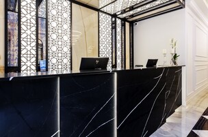 Una mesa de recepción con diseño de mármol negro, dos computadoras portátiles y un jarrón con flores.