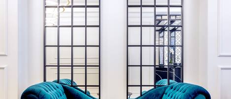 Una habitación con un sofá de terciopelo color turquesa, una mesa de mármol negro y dos ventanas de arco con marcos negros.