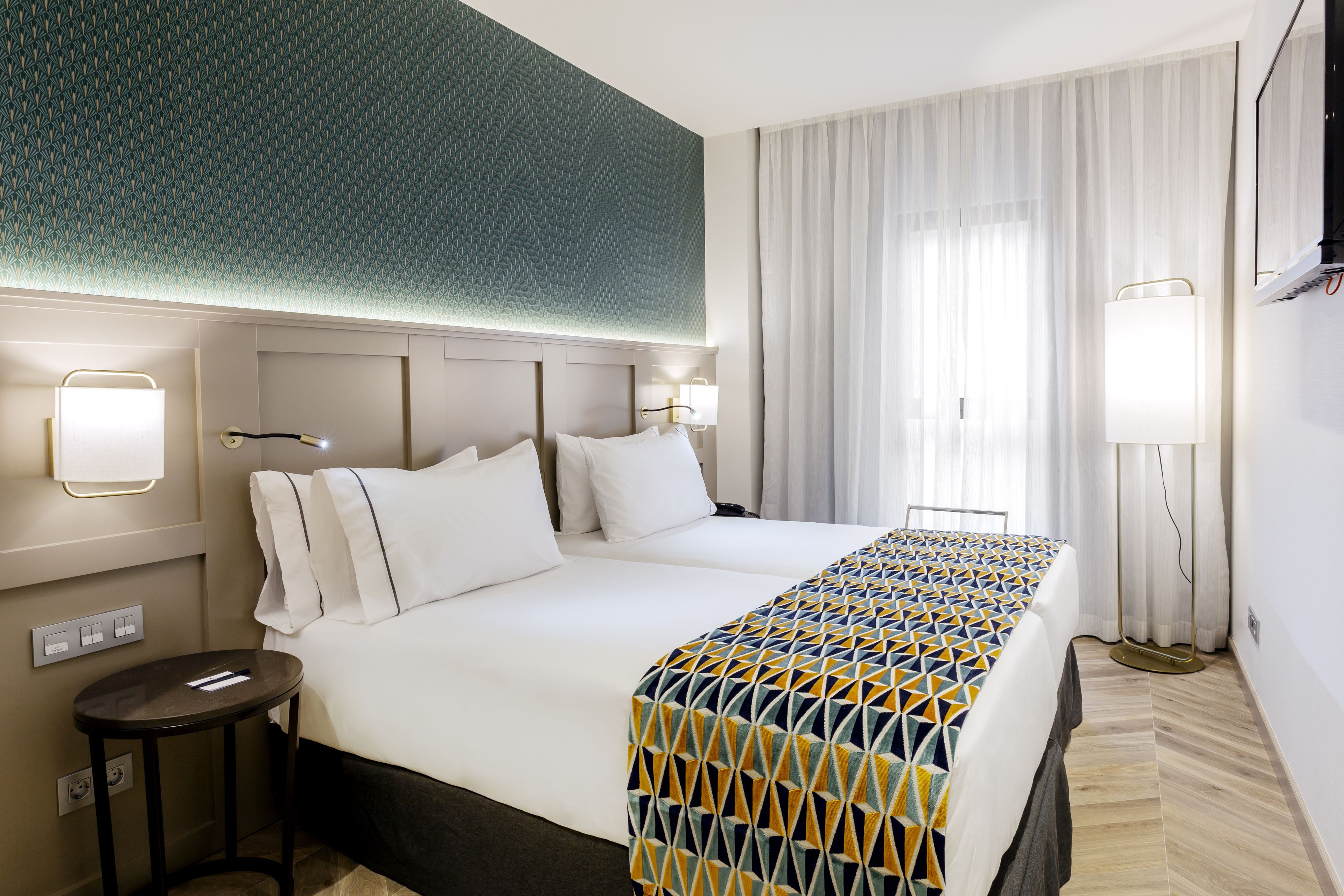 Une chambre d’hôtel avec un grand lit, une table de chevet, une lampe et un mur décoré d’un motif.