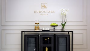 A reception desk with a logo for Eurostars Hotels, a water feature, a fruit display, and a vase with white flowers. - Eurostars Puerta Real Hotel (Granada)