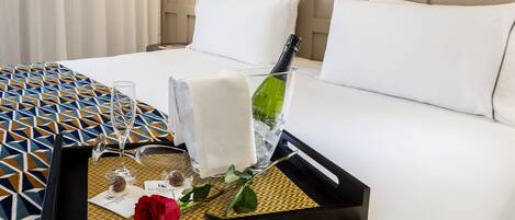 A hotel room with a bed, a tray with a bottle, glasses, and a rose.