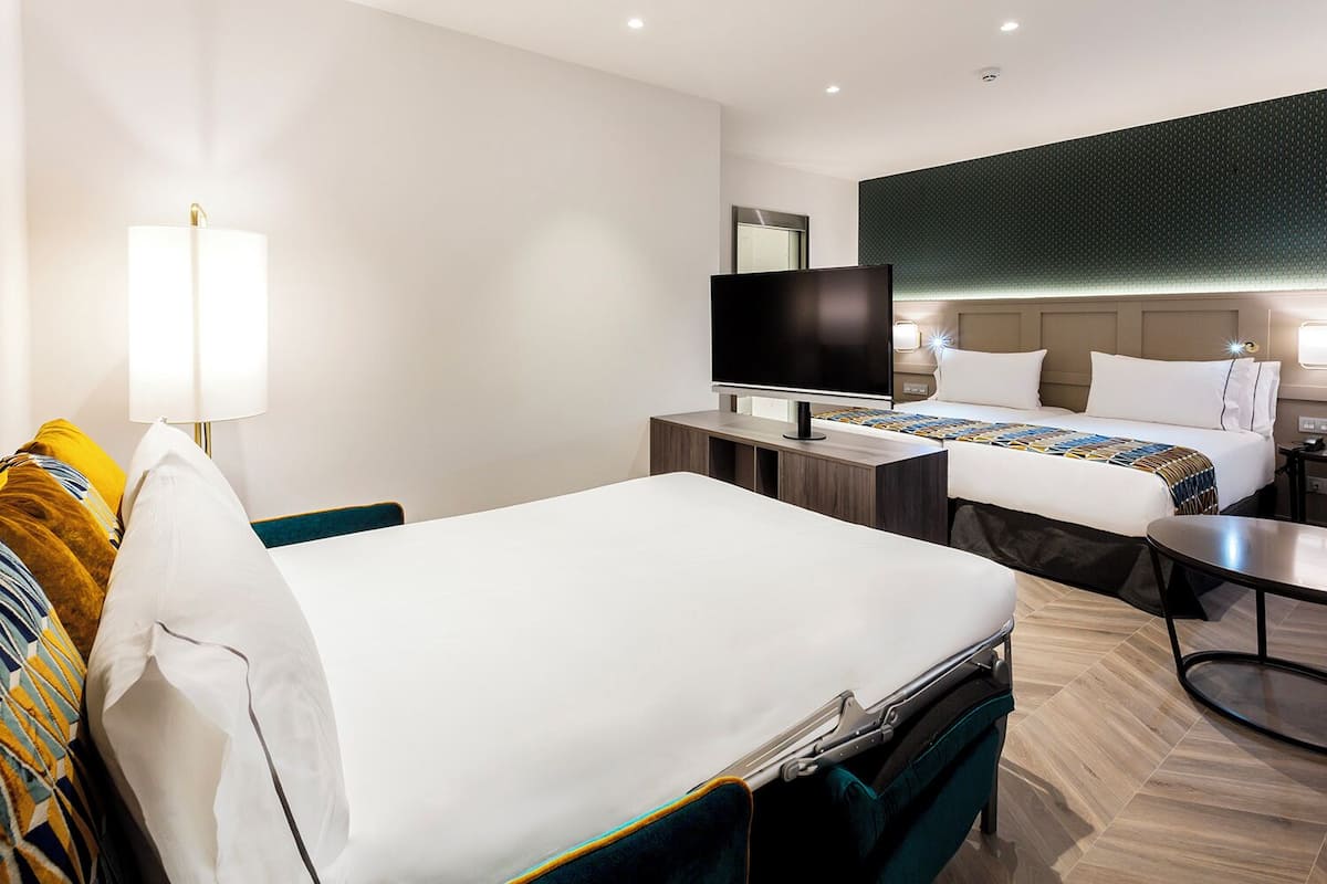 A hotel room with two beds, a TV, a desk, and a lamp.