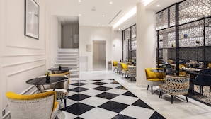 A modern hotel lobby with a checkered floor, a staircase, and a seating area with yellow chairs and tables. - Eurostars Puerta Real Hotel (Granada)