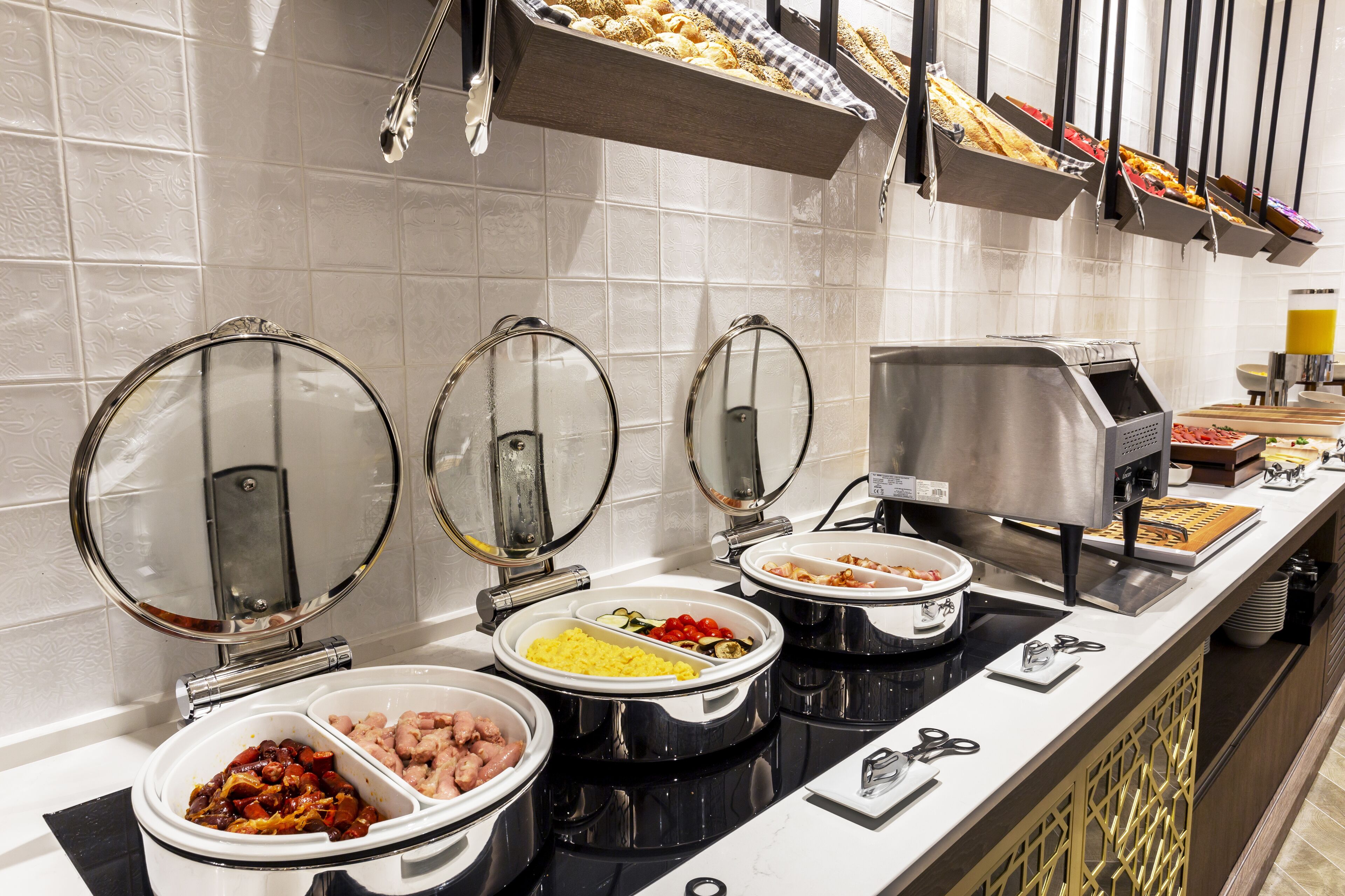 Ein reichhaltiges Buffet mit verschiedenen Speisen in Schalen und Behältern, einer Kaffeemaschine und Besteck auf einer Theke.