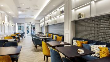 A modern restaurant interior with high tables, blue and yellow upholstered seating, and patterned wall decor.