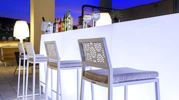Zona de bar con sillas blancas y una barra que exhibe botellas y copas.