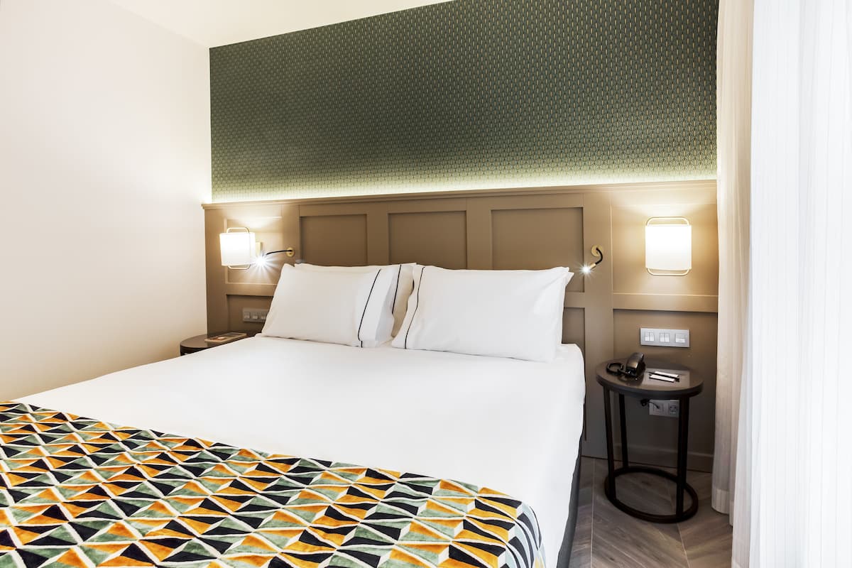 A hotel room with a large bed, two bedside lamps, a small table with a phone, and a patterned bedspread.