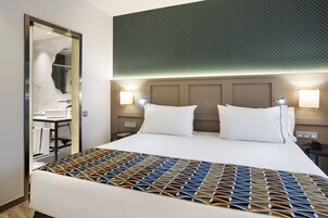 Una habitación de hotel con una cama grande, dos lámparas de noche, un espejo y una colcha estampada.