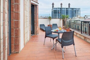 Een balkon met twee rieten stoelen, een klein rond tafeltje en een bloempot.