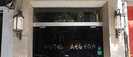 The entrance to a hotel with a glass door, a metal canopy, and a sign that reads "HOTEL AEGON."