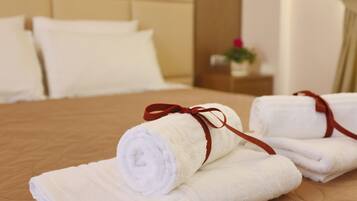 A neatly made bed with white towels and a red ribbon, a wooden headboard, and a small bedside table with a plant.