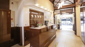 A reception area with a wooden reception desk, a digital screen, and a glass door leading outside. - Aegeon Hotel (Thessaloniki)
