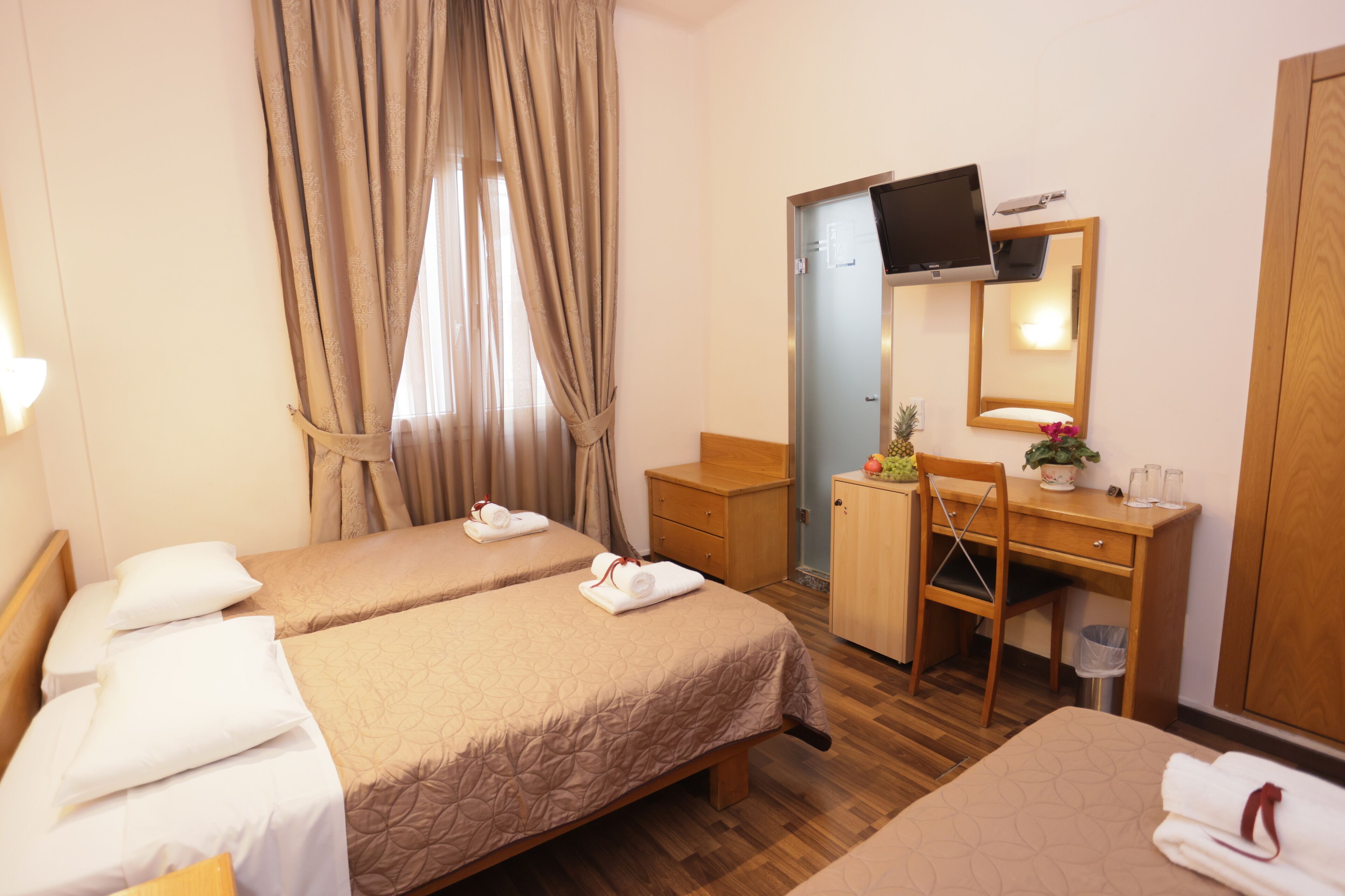 A hotel room with two beds, a desk, a mirror, and a television.