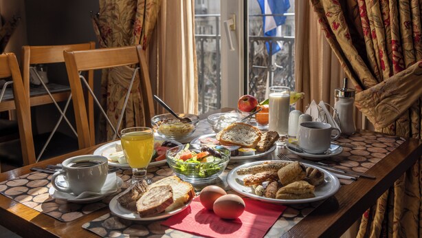 A breakfast table with plates of food, a coffee cup, and a glass of orange juice. - Aegeon Hotel (Thessaloniki)
