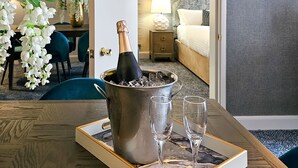 Habitación de hotel con comedor, cama y mesita de noche con lámpara.
