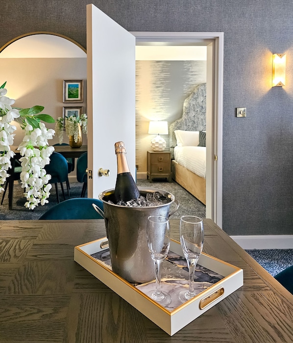 A hotel room with a dining area, a bed, and a nightstand with a lamp.