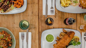 A wooden table with various dishes including fish and chips, fries, and a burger.