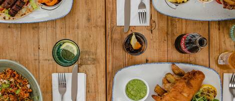 A wooden table with various dishes including fish and chips, fries, and a burger.