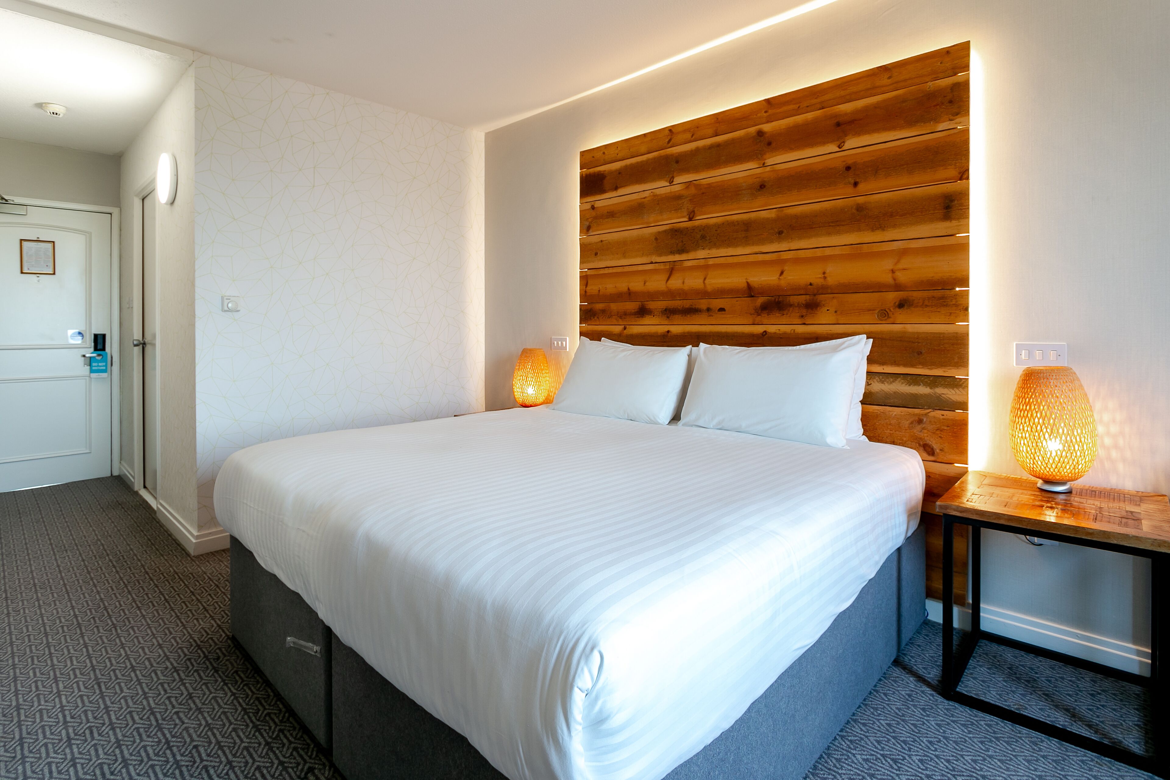 Un lit bien fait, avec des draps blancs, une tête de lit en bois et deux lampes de chevet.