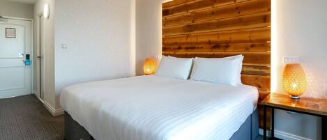 Una cama bien hecha con sábanas blancas, cabecera de madera y dos lámparas de noche.
