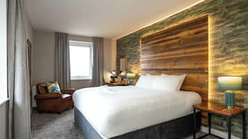 A modern hotel room with a large bed, a wooden accent wall, a desk with a lamp, and a chair.