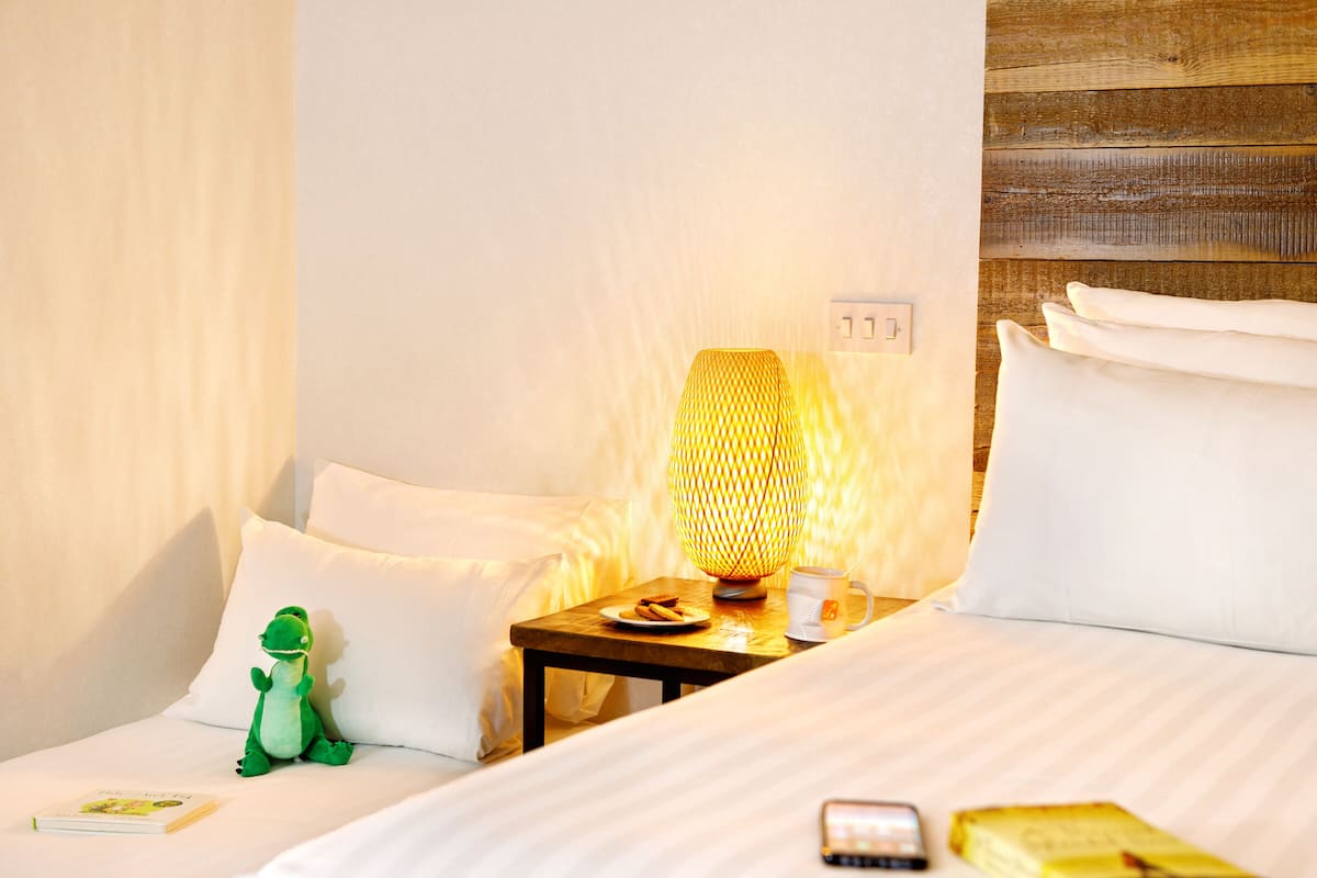 Een netjes opgemaakt bed met wit beddengoed, een nachtkastje met een lamp, een zacht groen knuffeldier en een boek.