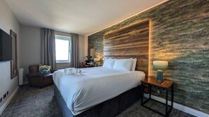 Una habitación de hotel con una cama grande, un escritorio, una silla, un espejo, una ventana con cortinas y una pared con textura.