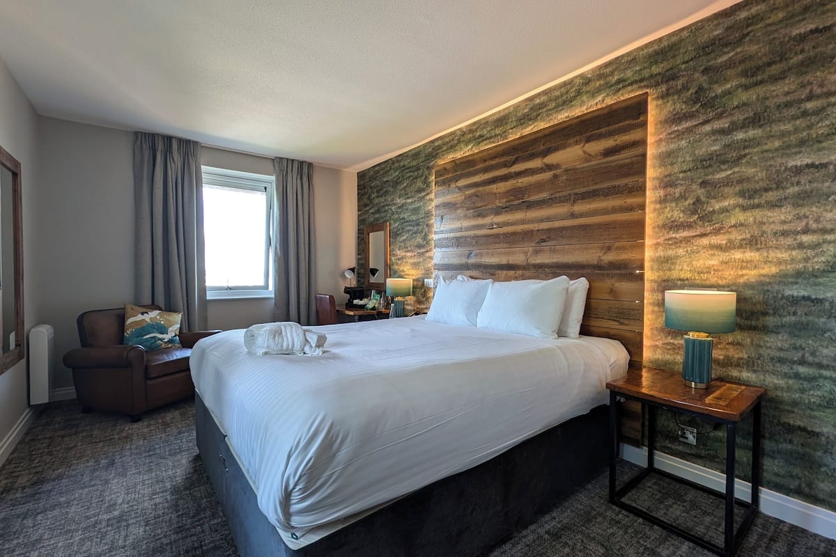 Hotelkamer met een groot bed, een bureau, een stoel, een spiegel, een raam met gordijnen en een structuurwand.