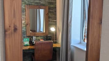 Una habitación acogedora con un sillón de cuero marrón, un escritorio de madera, un espejo y una ventana con cortinas.