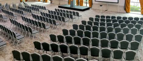 A conference room with rows of chairs, a stage with a podium, and a large screen.