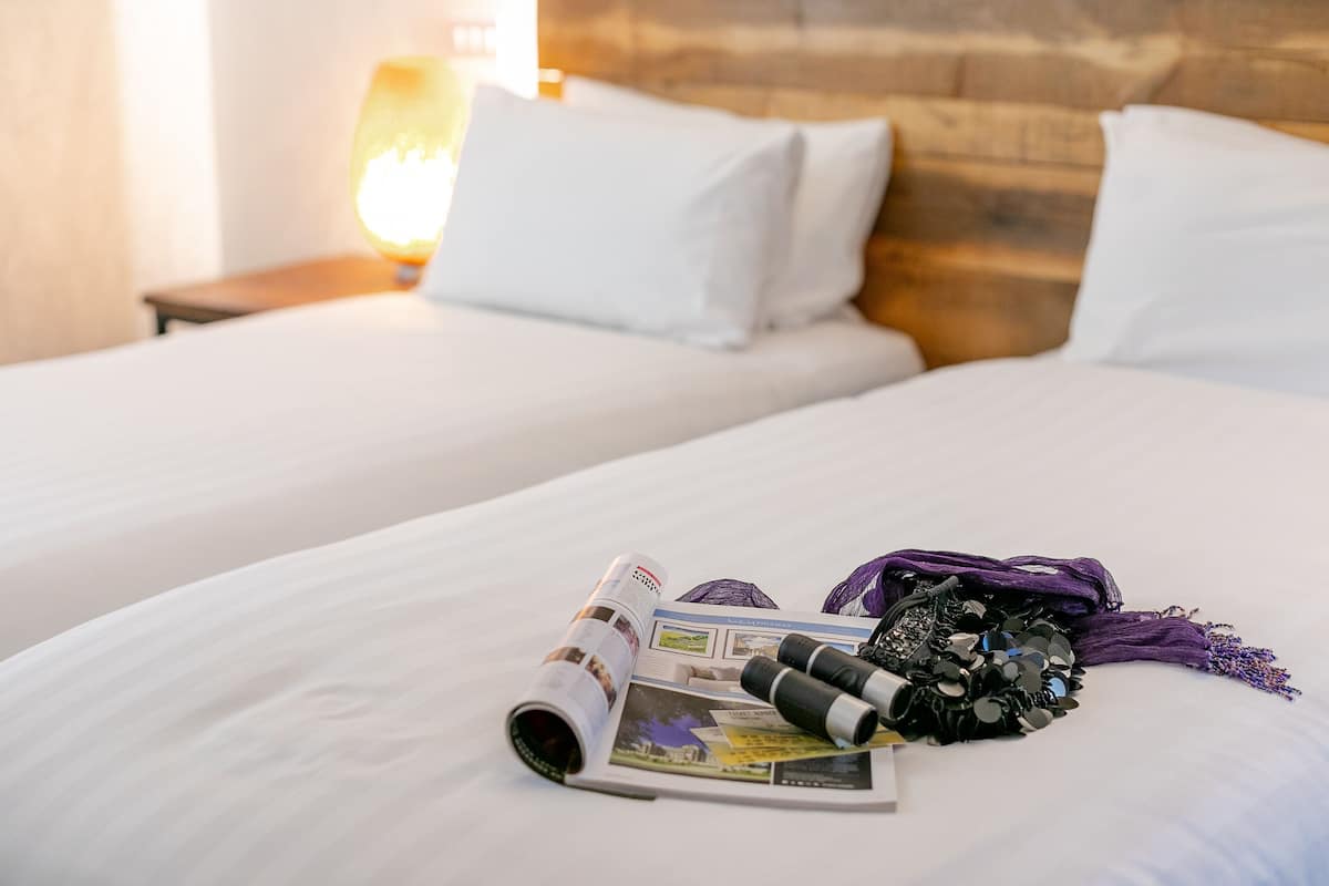 Een hotelkamer met twee bedden, een lamp en een tijdschrift op het bed.