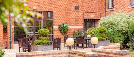 An outdoor patio area with brick walls, wooden furniture, and potted plants.