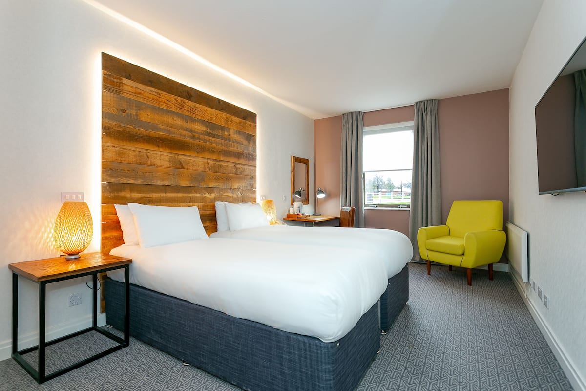 Een hotelkamer met een groot bed, een houten accentmuur, een bedlampje, een stoel en een televisie.