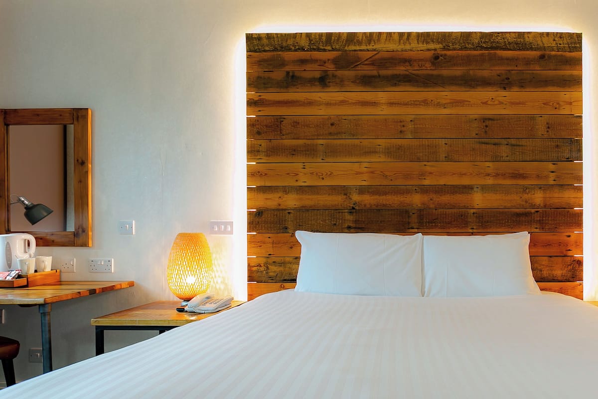Een hotelkamer met een houten hoofdeinde, een bed met witte lakens, twee bedlampjes, een kleine tafel met een telefoon en een koffiezetapparaat.