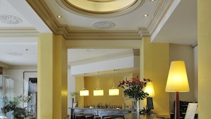 A reception area with a curved counter, bar stools, and a vase with flowers. - Hotel Roger de Lluria Barcelona (Barcelona)