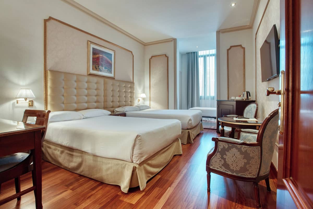A hotel room with two beds, a desk, a chair, a television, and a window with curtains.