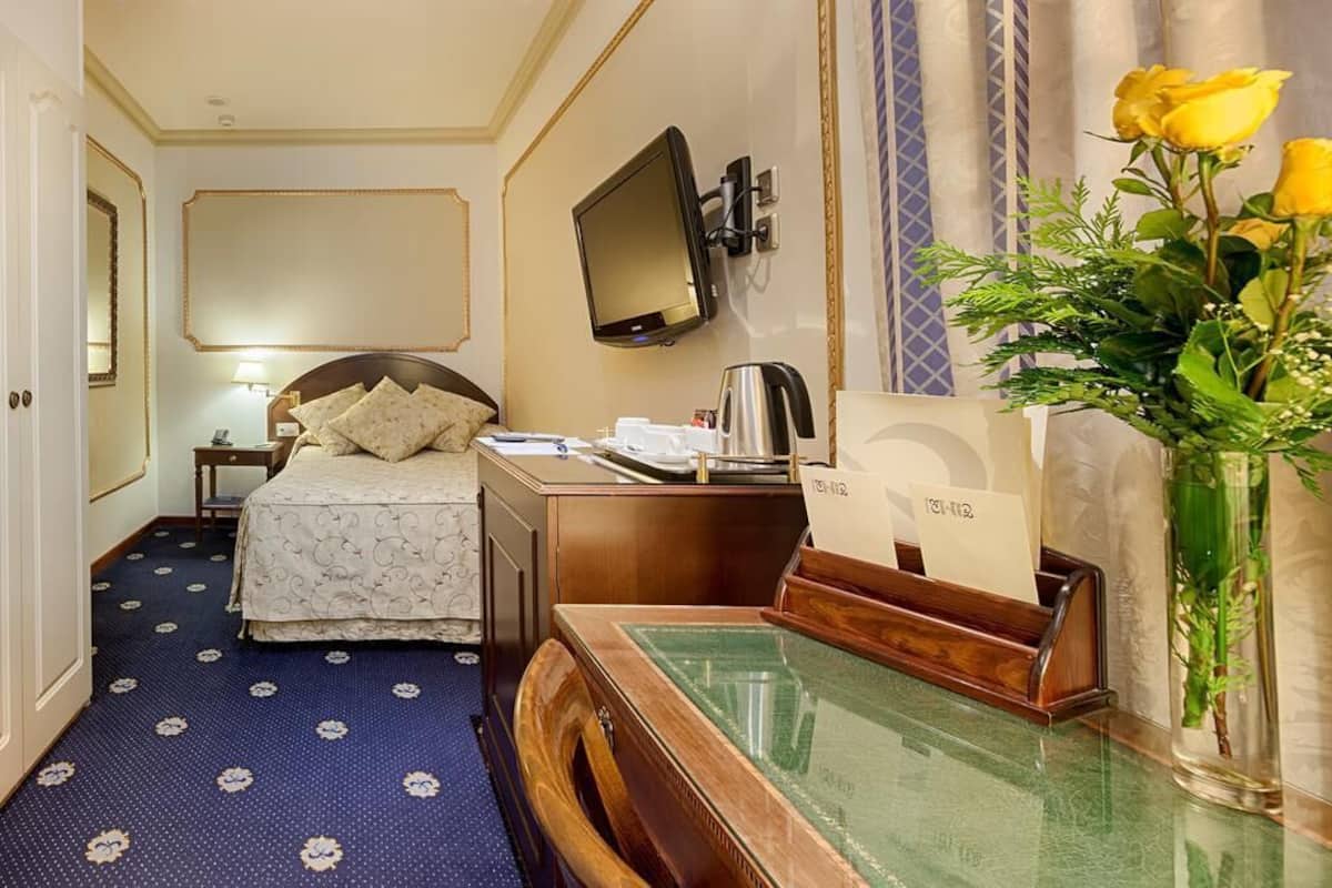 Une chambre d’hôtel avec un lit, un bureau et une télévision. Un vase rempli de fleurs est posé sur le bureau.