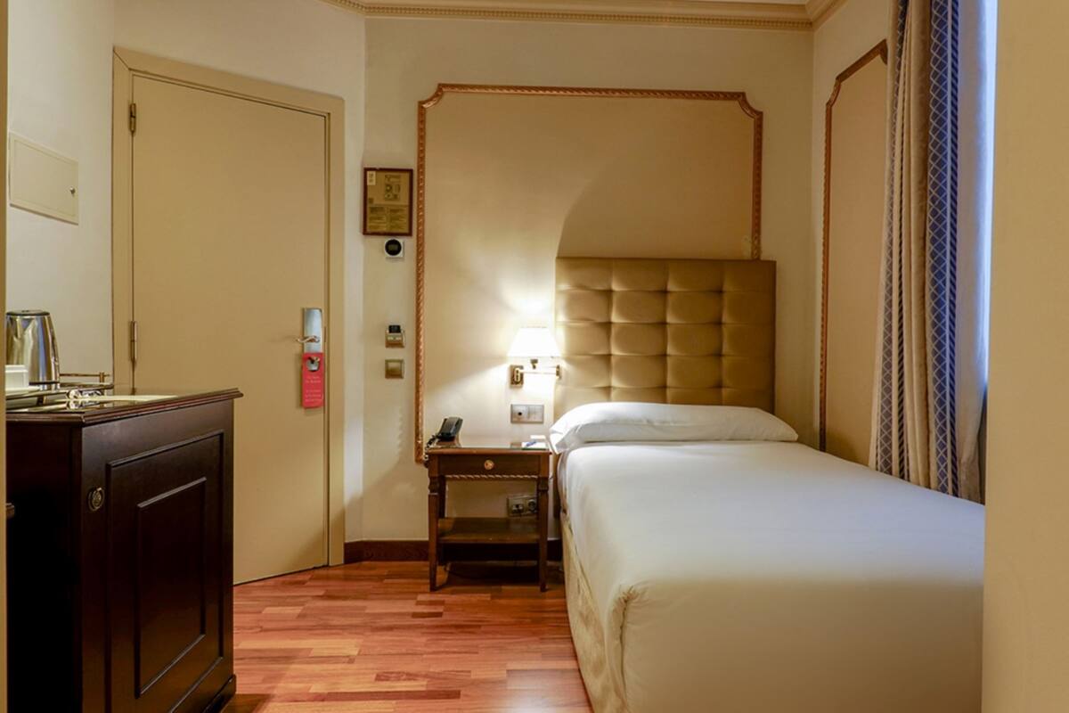 A hotel room with a bed, a nightstand, a lamp, a wardrobe, and a door.