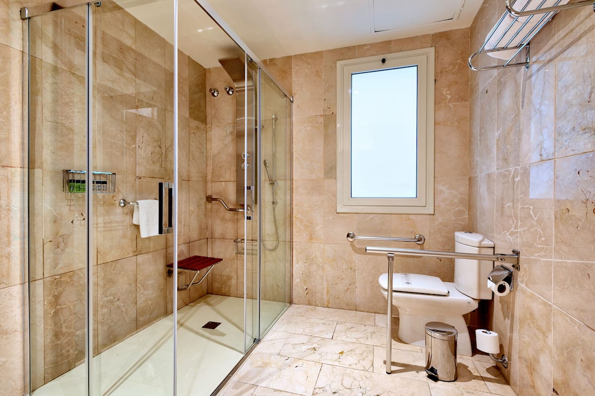 A modern bathroom with a glass shower enclosure, a toilet with a grab bar, and a window providing natural light.