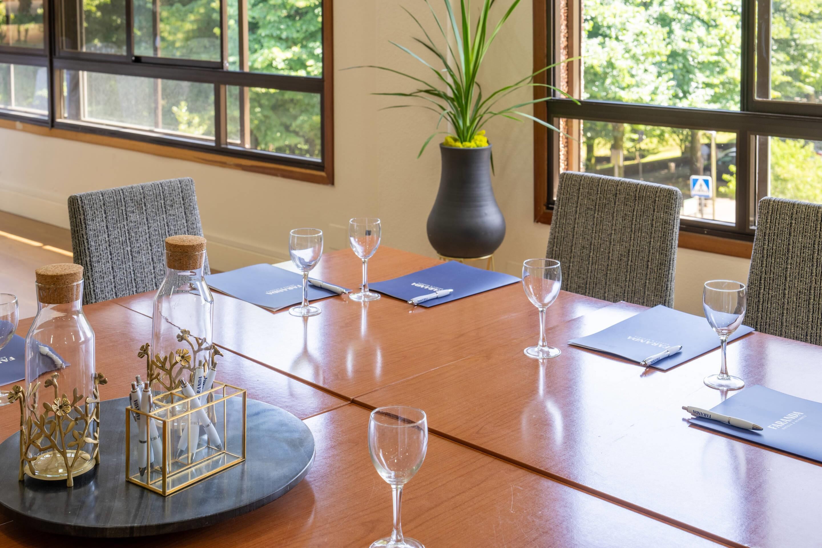 Une table de conférence, avec des chaises, des verres à vin et des documents.