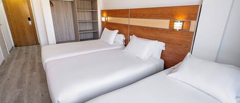 A hotel room with two beds, a wooden headboard, a wardrobe, and a bedside lamp.