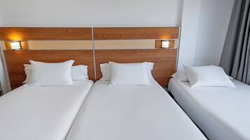 A hotel room with three single beds, wooden headboard, and bedside lamps.