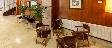 Eine Lobby mit holzverkleideten Wänden, einer Treppe und Ledersesseln um einen Glastisch mit Blumen.