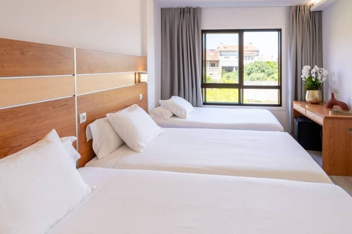 Ein Hotelzimmer mit zwei Betten, einem Holzkopfteil, einem Schreibtisch mit Blumen in einer Vase und einem Fenster mit Vorhängen.